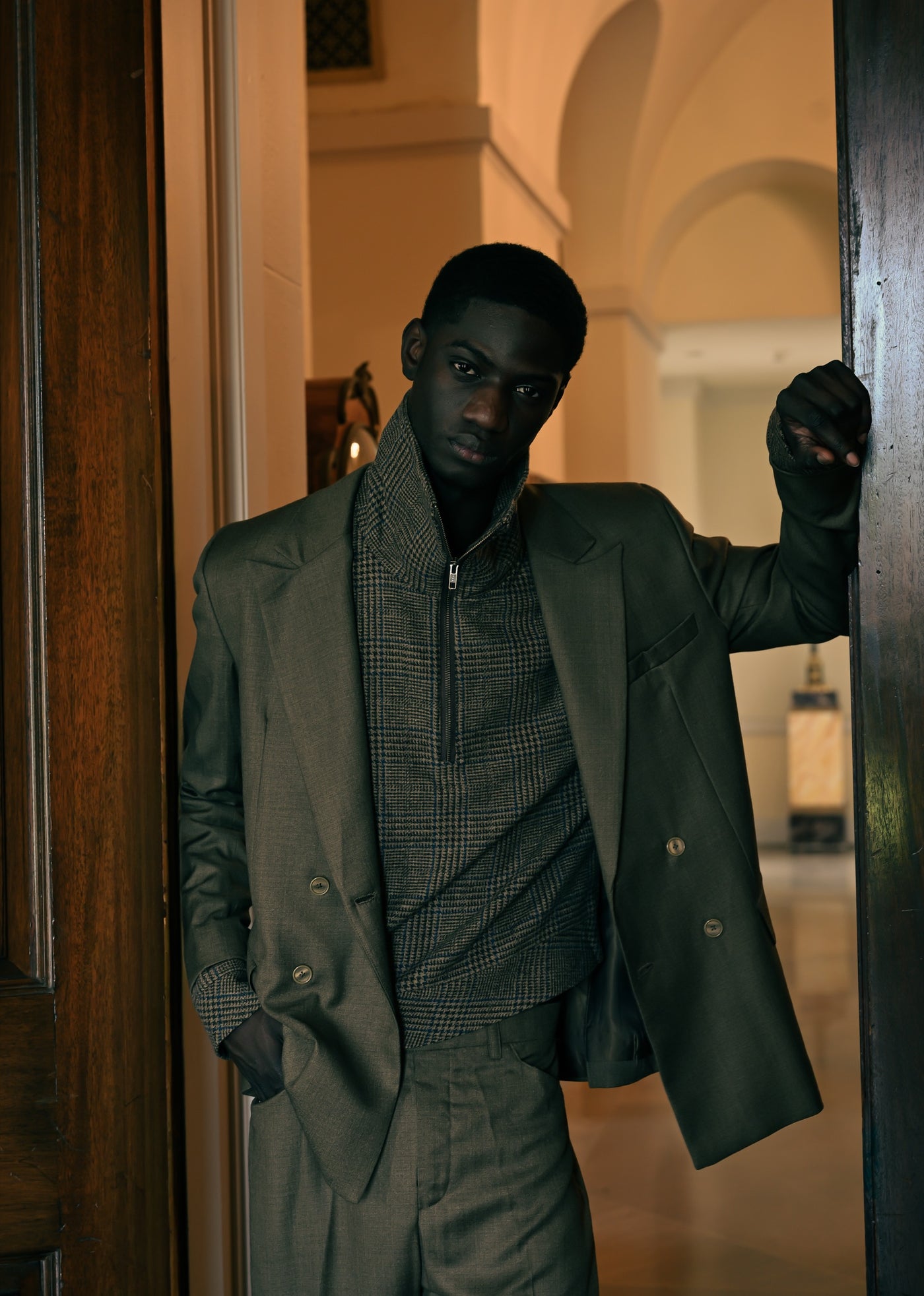 Pierre Blanc Autumn Winter 2026-27 campaign - olive double-breasted suit in a stone archway